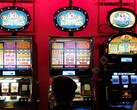 Machines à sous à l'intérieur d'un casino avec des écrans lumineux et des personnes jouant devant (Image source : djedj via Pixabay)